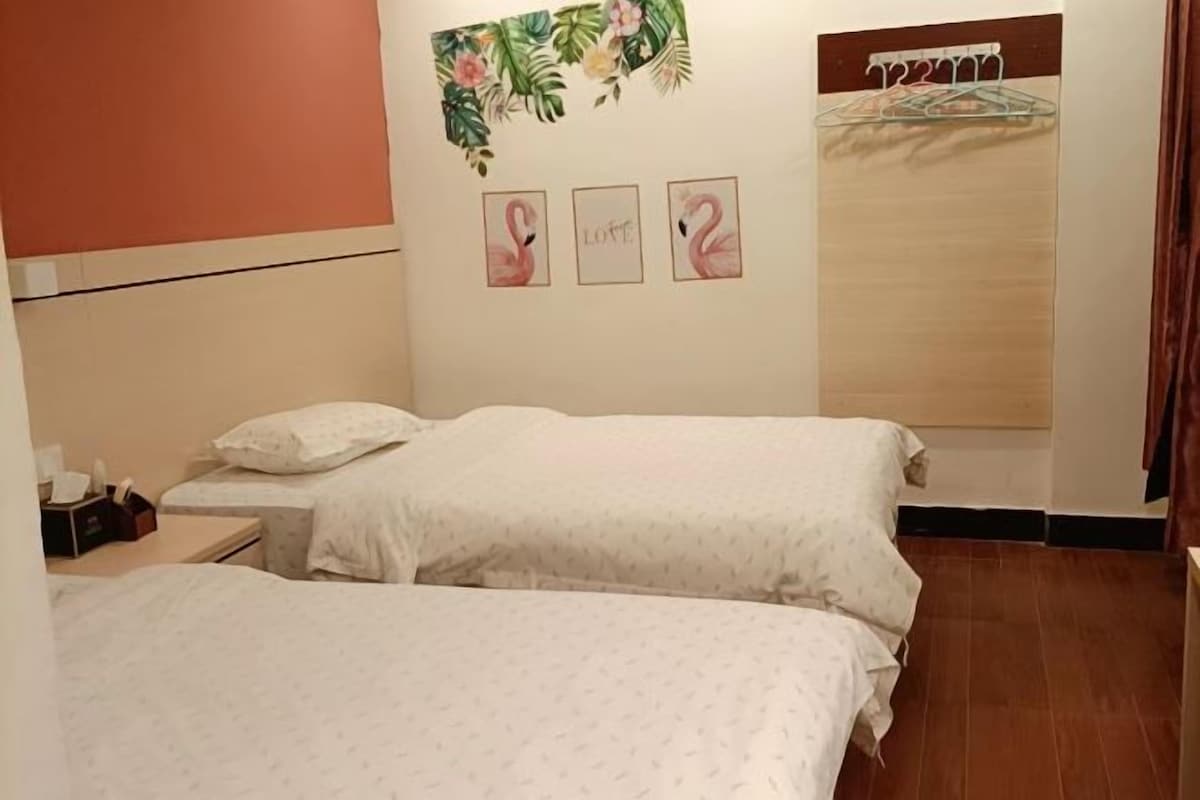 A room with two beds, a small table, and a wall with three framed pictures.