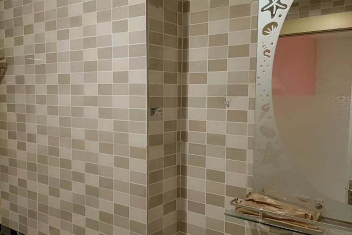Un bagno con piastrelle beige e bianche a scacchi, un box doccia in vetro e un portasciugamani con un asciugamano rosa.