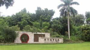 A sign for Mei Hua Urban Garden with a stone wall and a palm tree in the background. - Longxiang Hotel (Zhuhai)