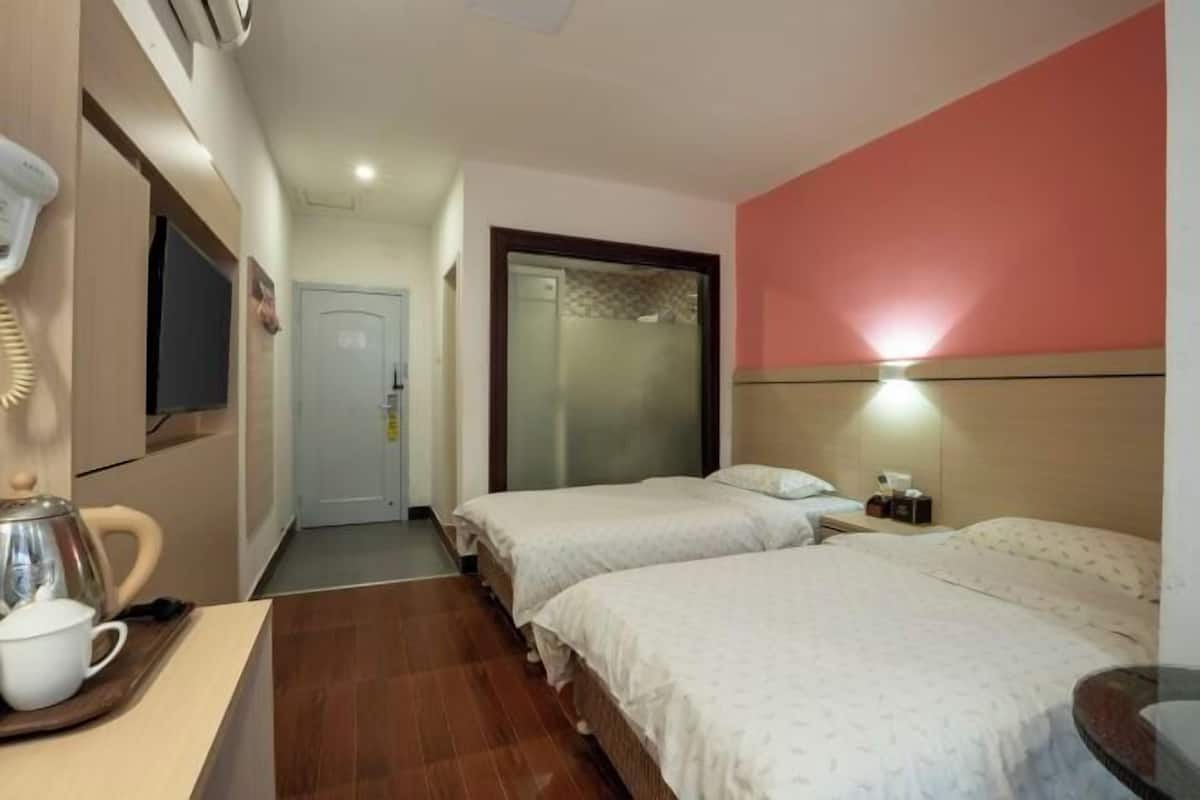 A hotel room with two beds, a TV, a coffee maker, and a wall-mounted light.