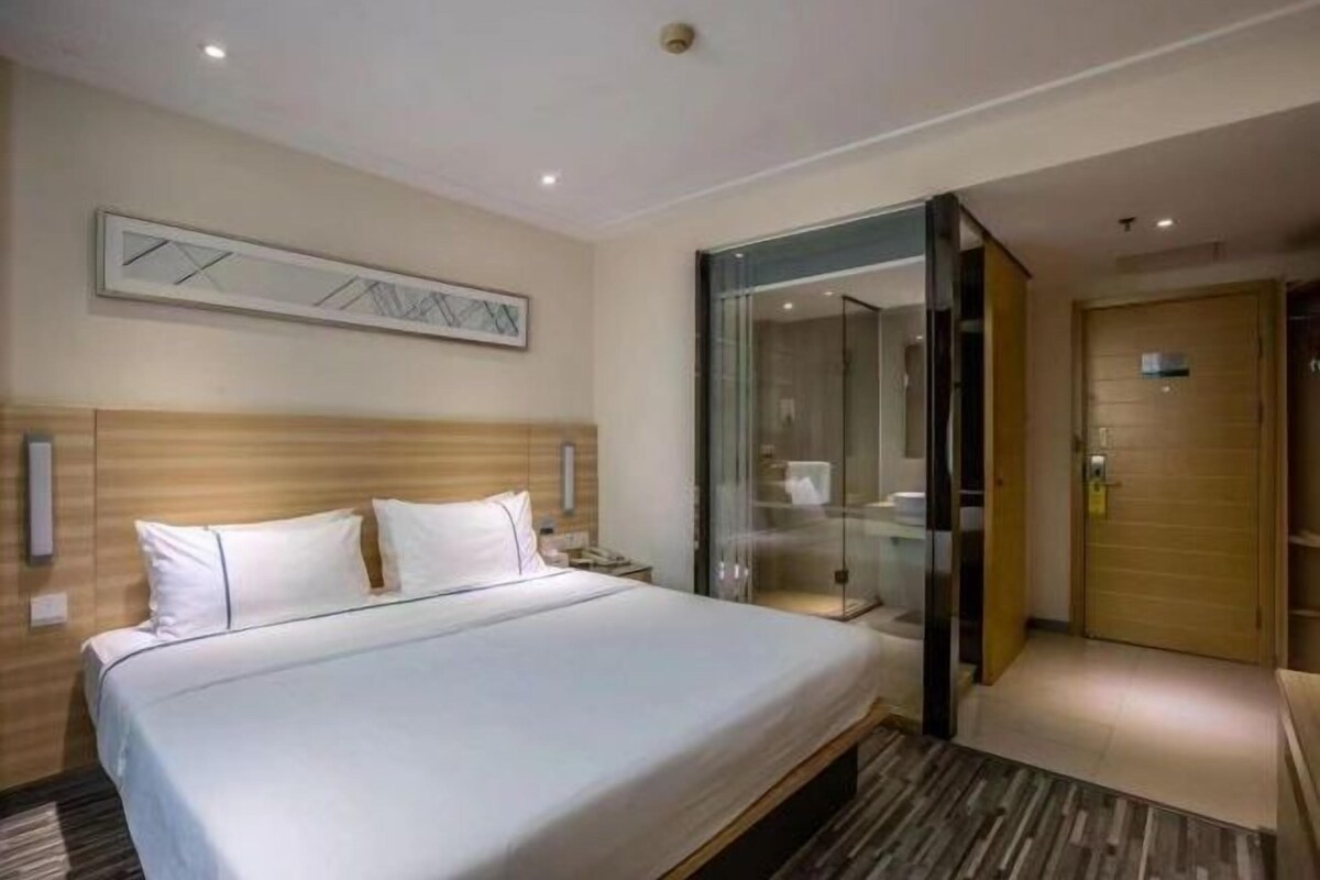Habitación de hotel con una cama grande, un separador de vidrio, un cabecero de madera y una lámpara moderna.