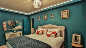 A bedroom with a tufted headboard, a large bed with a dark patterned bedspread, a small bedside table with a framed picture, and a wall-mounted mirror with decorative elements. - Luxury Boutique 2 Bed Apartment in the heart of Bowness on Windermere (Bowness-on-Windermere)