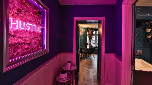 A hallway with a neon sign reading "HUSTLE" on a brick wall, leading to a dining area with a chandelier and a small round table. - Luxury Boutique 2 Bed Apartment in the heart of Bowness on Windermere (Bowness-on-Windermere)