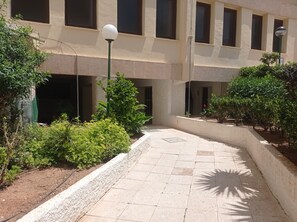 Stroll through this serene courtyard, lined with lush greenery and surrounded by a charming building with multiple windows.