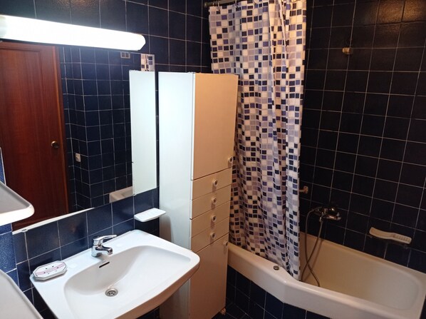 A bathroom with a white sink, a mirror, a white cabinet, a shower curtain with a checkered pattern, and a bathtub.