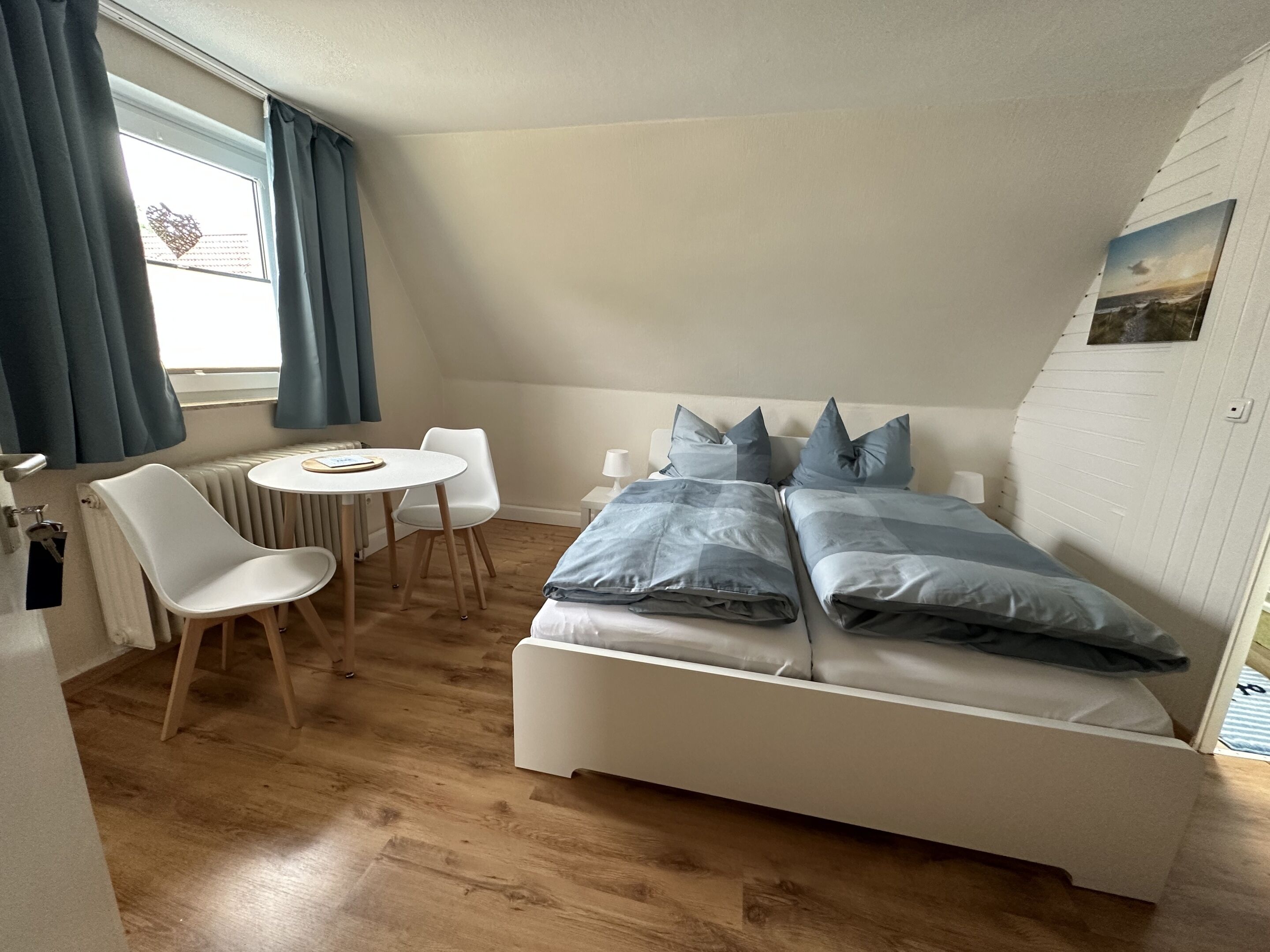 Une petite chambre à coucher moderne, avec un lit blanc, deux oreillers, une petite table ronde et une chaise.