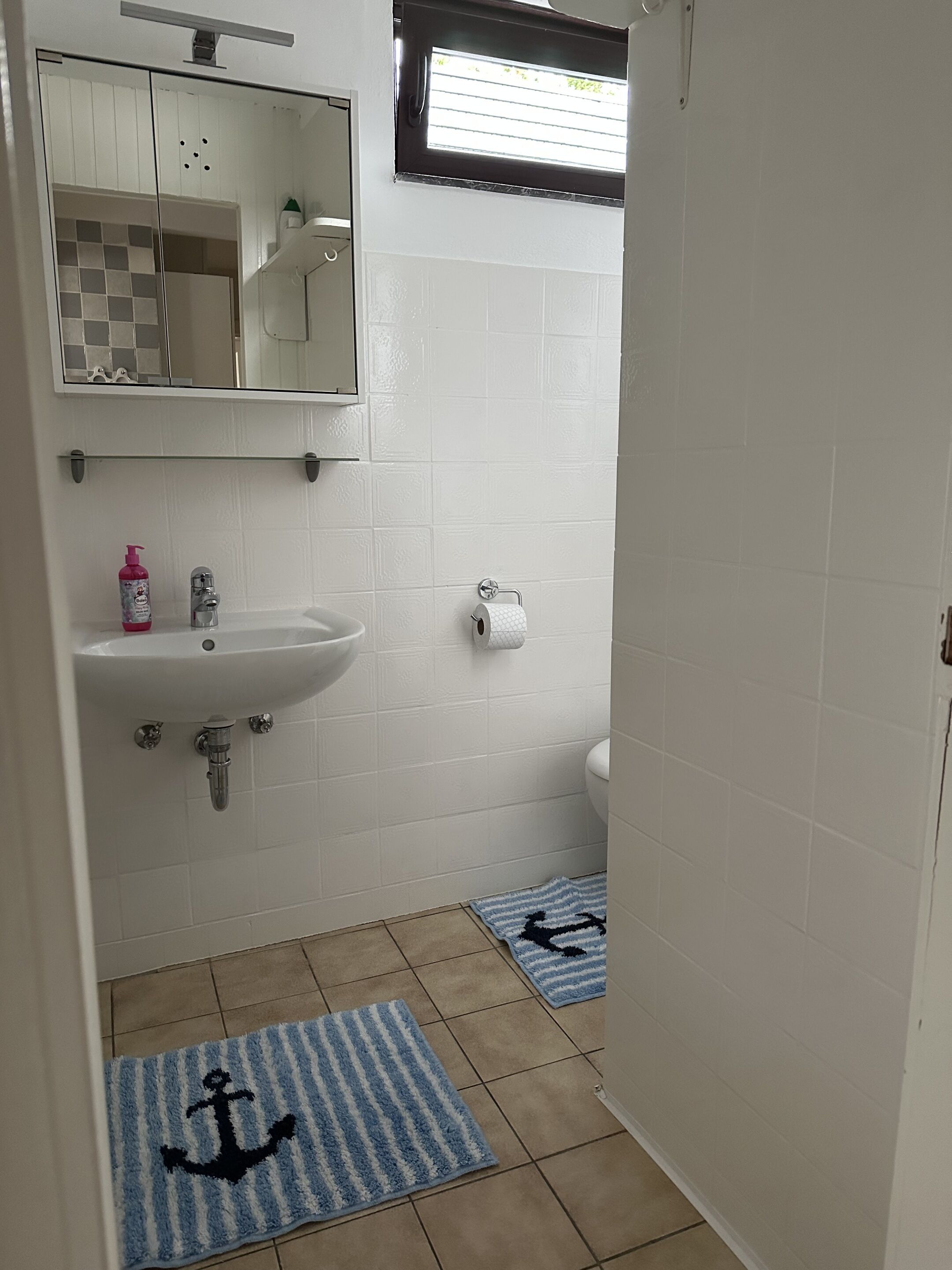 A bathroom with a white sink, a mirror, a toilet, and two striped rugs on the floor.