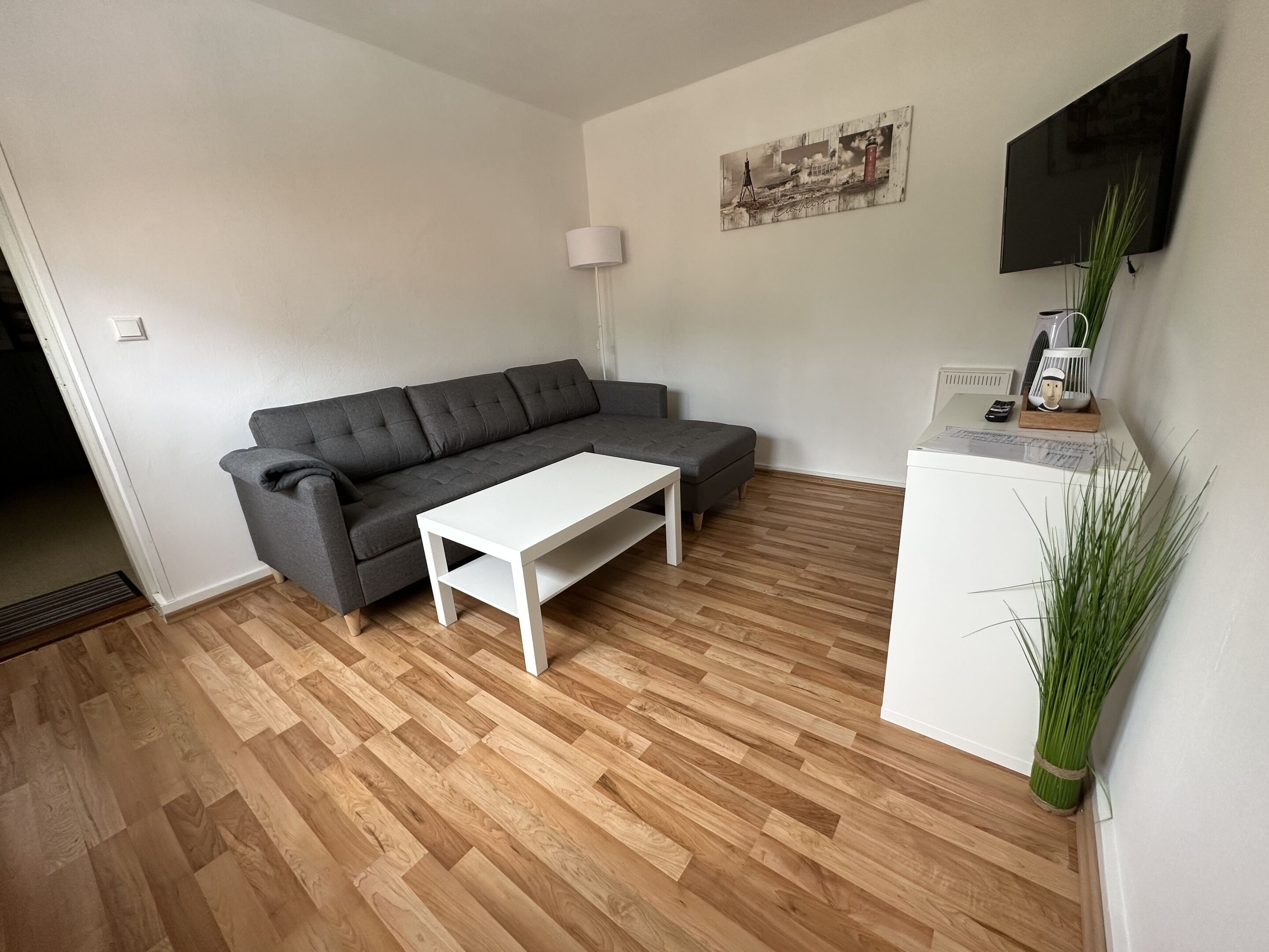 Ein modernes Wohnzimmer mit einem grauen Sofa, einem weißen Couchtisch und Holzboden.