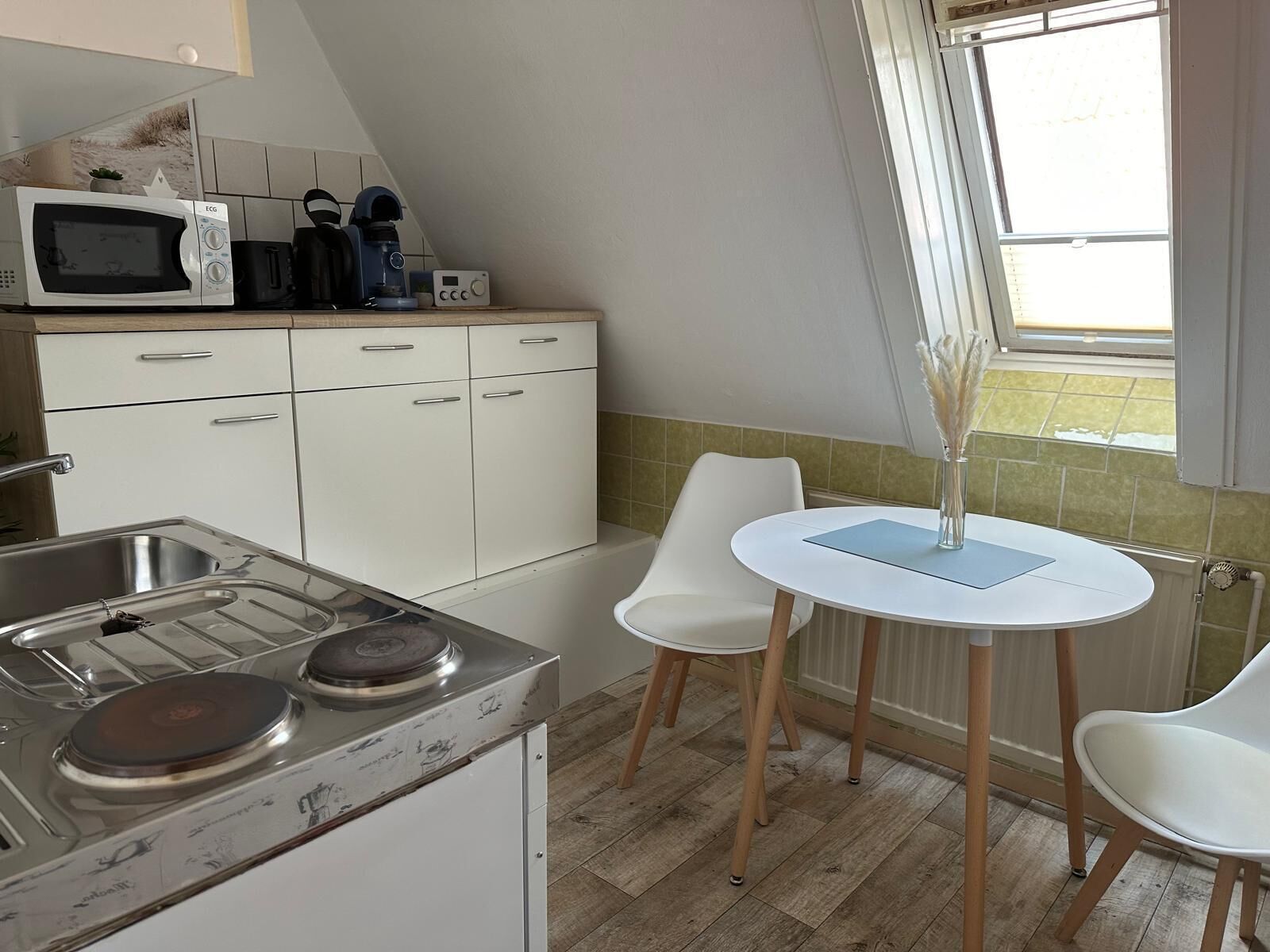 Een kleine keuken met een magnetron, koffiezetapparaat en een eettafel met stoelen.