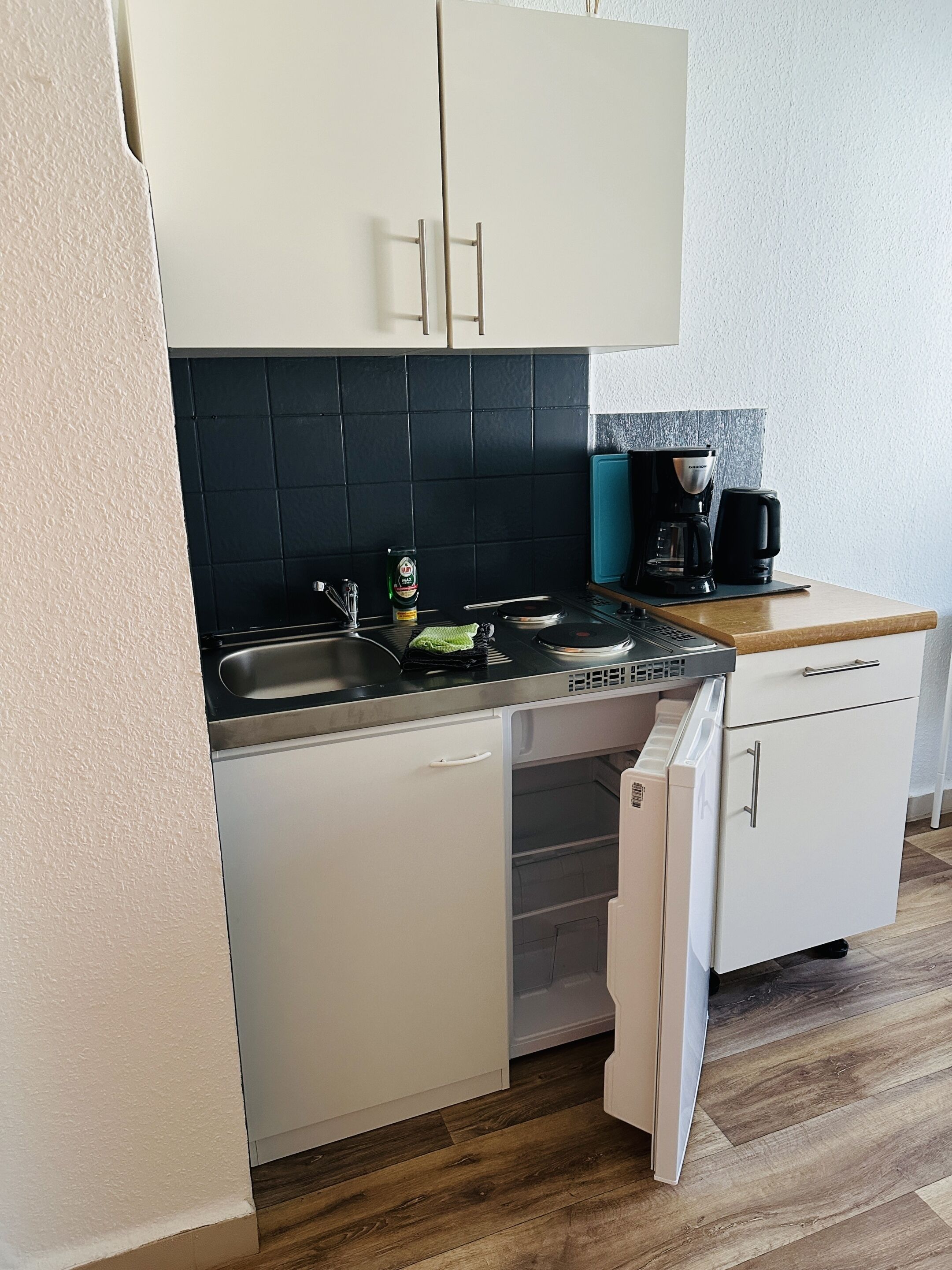 Eine kompakte Küche mit schwarzem Fliesenrückwand, einer Kaffeemaschine und einem Geschirrspüler.