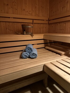 Puinen sauna, jossa on penkit ja erillinen penkki, jonka päällä on rullalle taiteltuja pyyhkeitä.