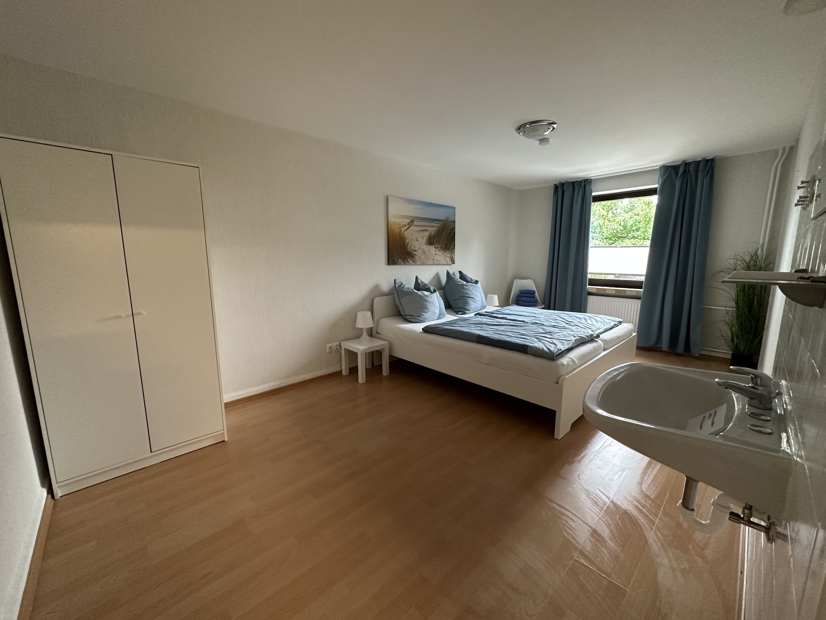 A bedroom with a bed, bedside table, lamp, and a view of the outdoors.
