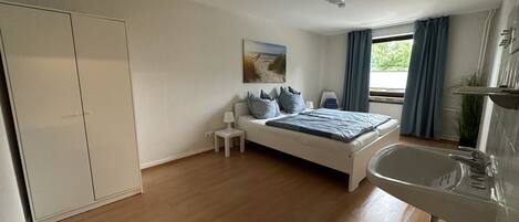 A bedroom with a bed, bedside table, lamp, and a view of the outdoors.