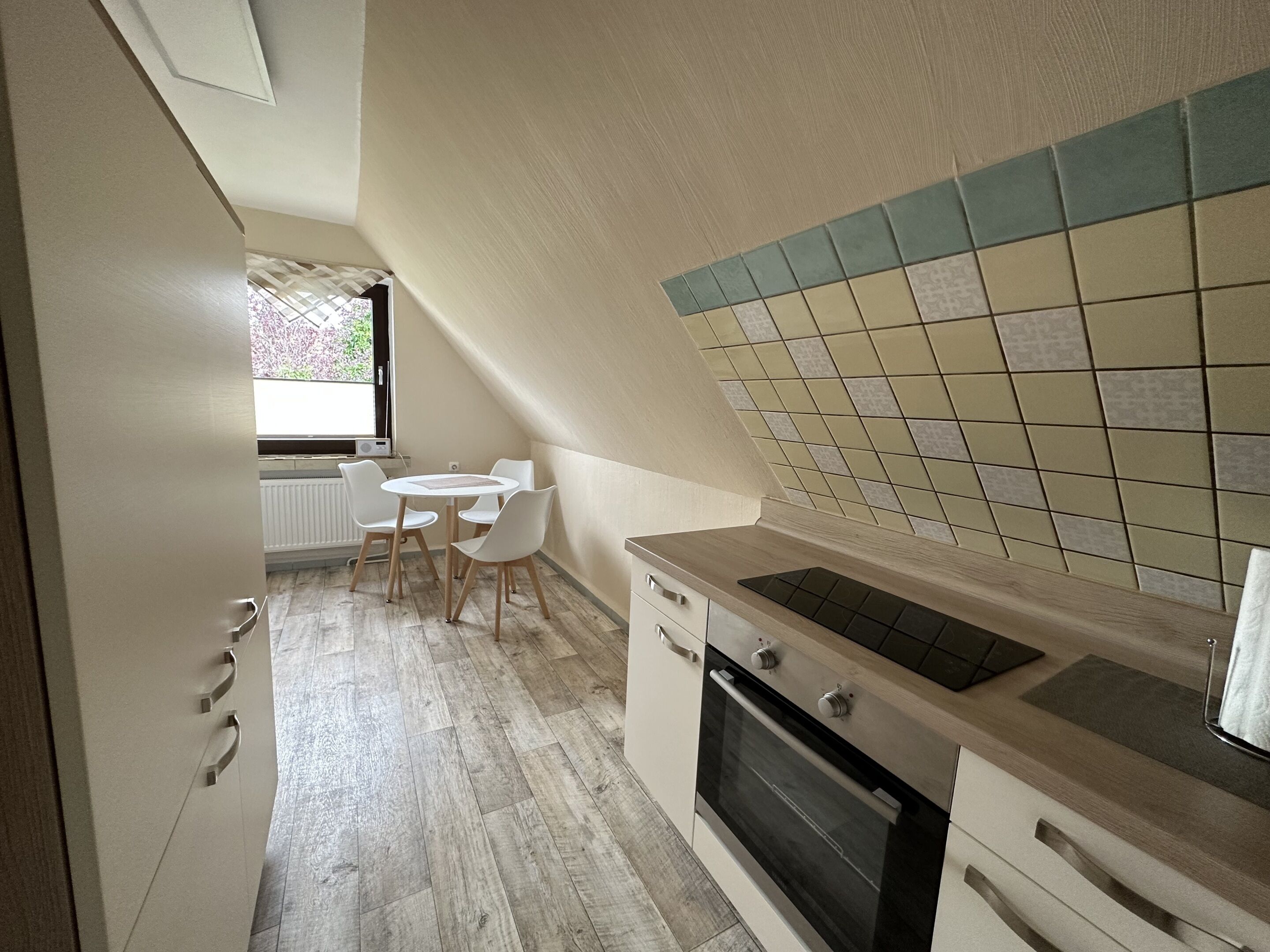 A modern kitchen with a dining area, featuring a tiled backsplash, a built-in oven, and a small round table with chairs.