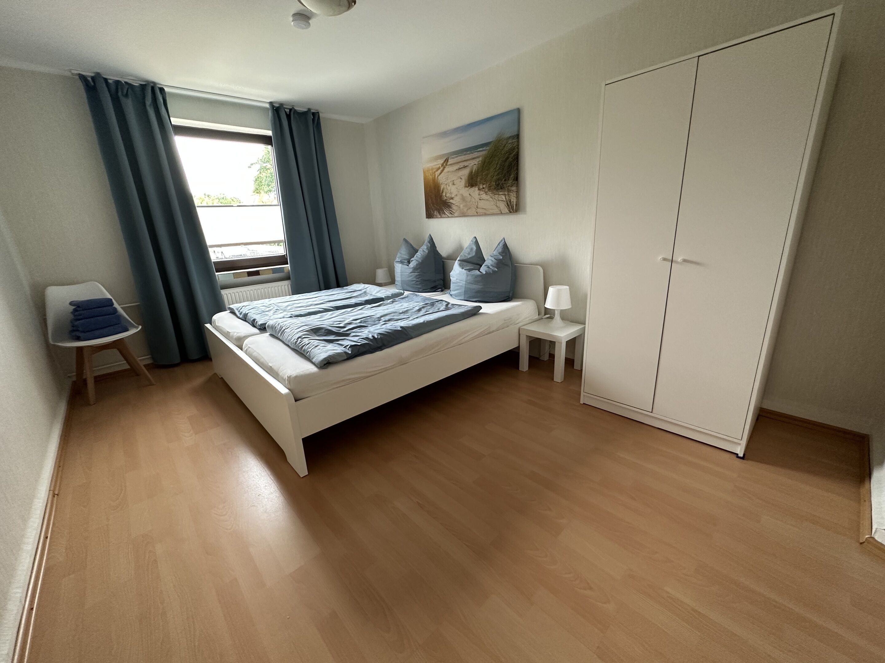 A bedroom with a bed, a bedside table, a lamp, a wardrobe, and a window with curtains.