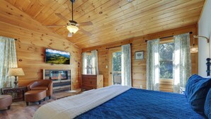 Een slaapkamer in een houten hut met een bed, een televisie, een open haard en een plafondventilator.