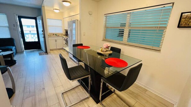 A modern kitchen with a glass dining table, black chairs, and a window with blinds. - Windward West 30 - Pool & 5 Minutes from the Beach (Cocoa Beach)