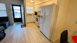 A compact kitchen with white cabinets, a refrigerator, and a microwave. There is a dining area with a table and chairs. - Windward West 30 - Pool & 5 Minutes from the Beach (Cocoa Beach)