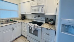 A compact kitchen with white cabinets, a built-in microwave, an oven, a sink, and a water dispenser. - Windward West 30 - Pool & 5 Minutes from the Beach (Cocoa Beach)