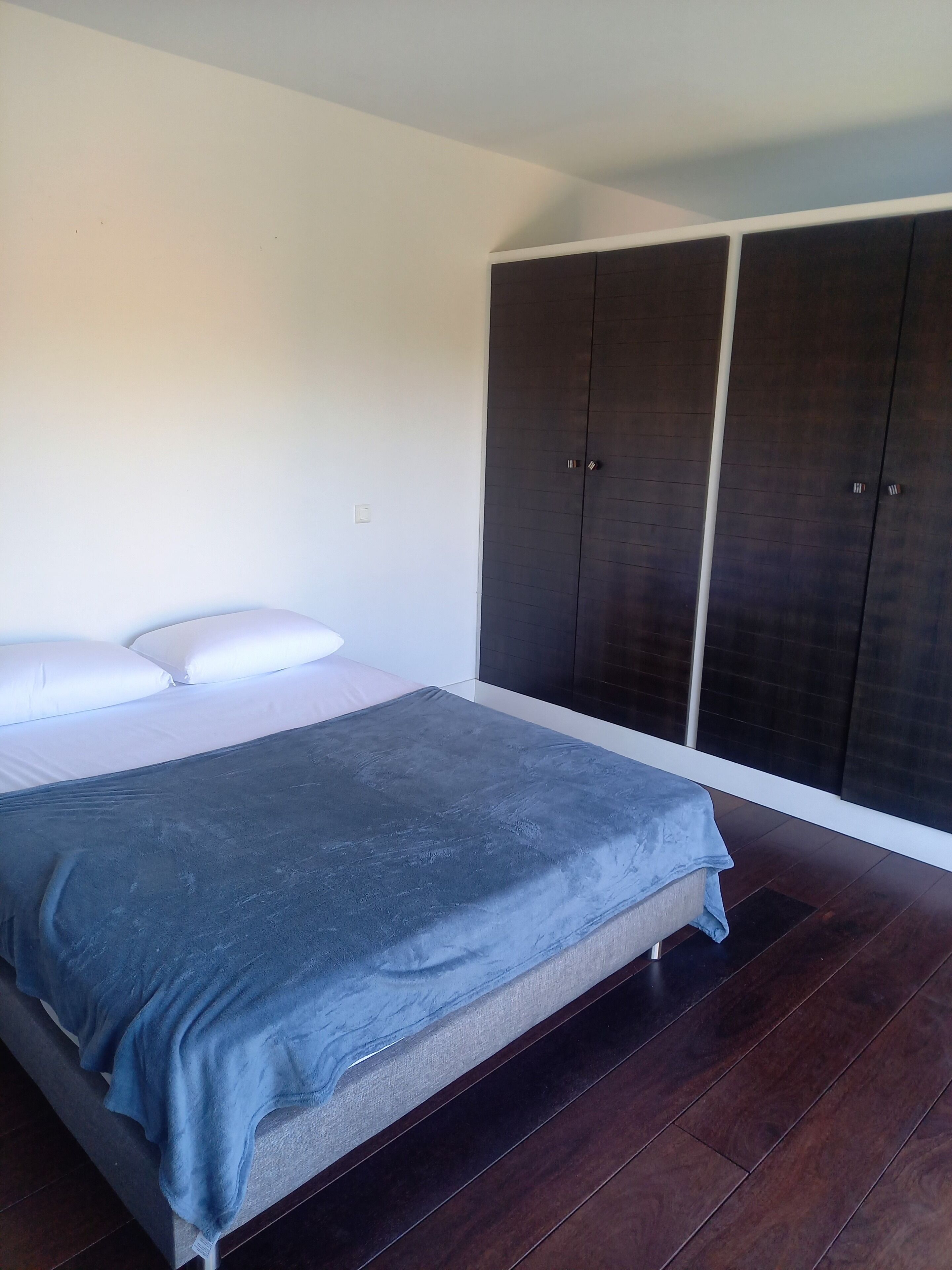A bedroom with a bed, a large wardrobe, and wooden flooring.