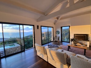 A spacious living room with a large sofa, a coffee table, and a fireplace. The room has large sliding glass doors leading to a balcony with a view of the sea. - Villa - Panoramic view of the Sanguinaires - Swimming pool (poti-chivari)