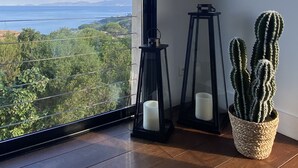 Una habitación con un ventanal grande, un espejo redondo, dos faroles negros y un cactus en una cesta tejida.