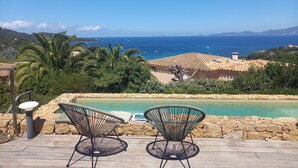 Zona de piscina con dos sillas, una piscina y vistas al mar y colinas.