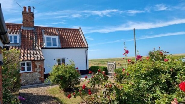 A two-story house with a red-tiled roof and white walls. - Detached 1-bed cottage overlooking the salt marshes (Salthouse)
