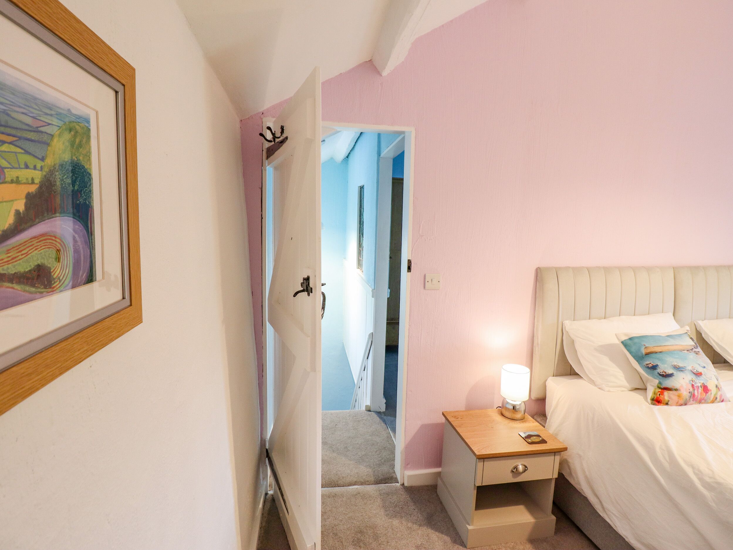 A bedroom with a bed, bedside table, and a door leading to another room.