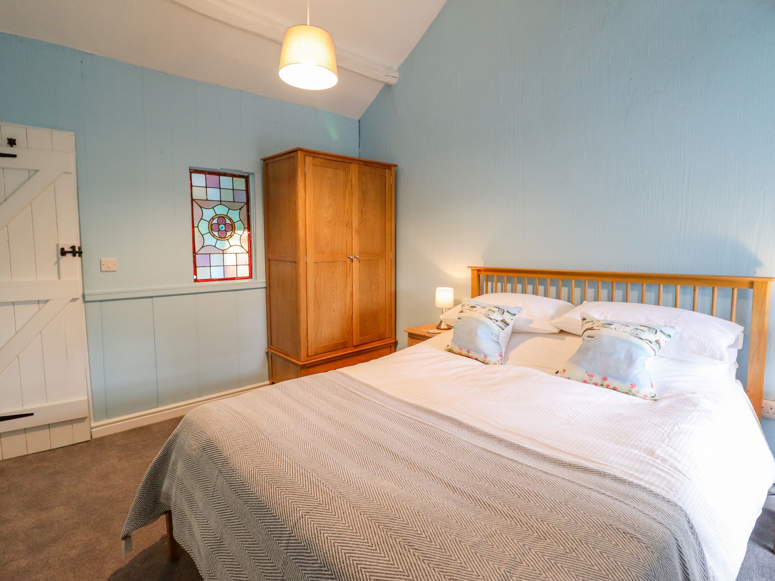 A bedroom with a bed, wooden wardrobe, and a nightstand with a lamp.