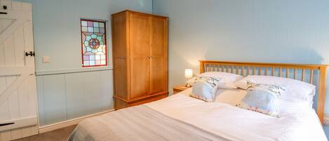 A bedroom with a bed, wooden wardrobe, and a nightstand with a lamp.