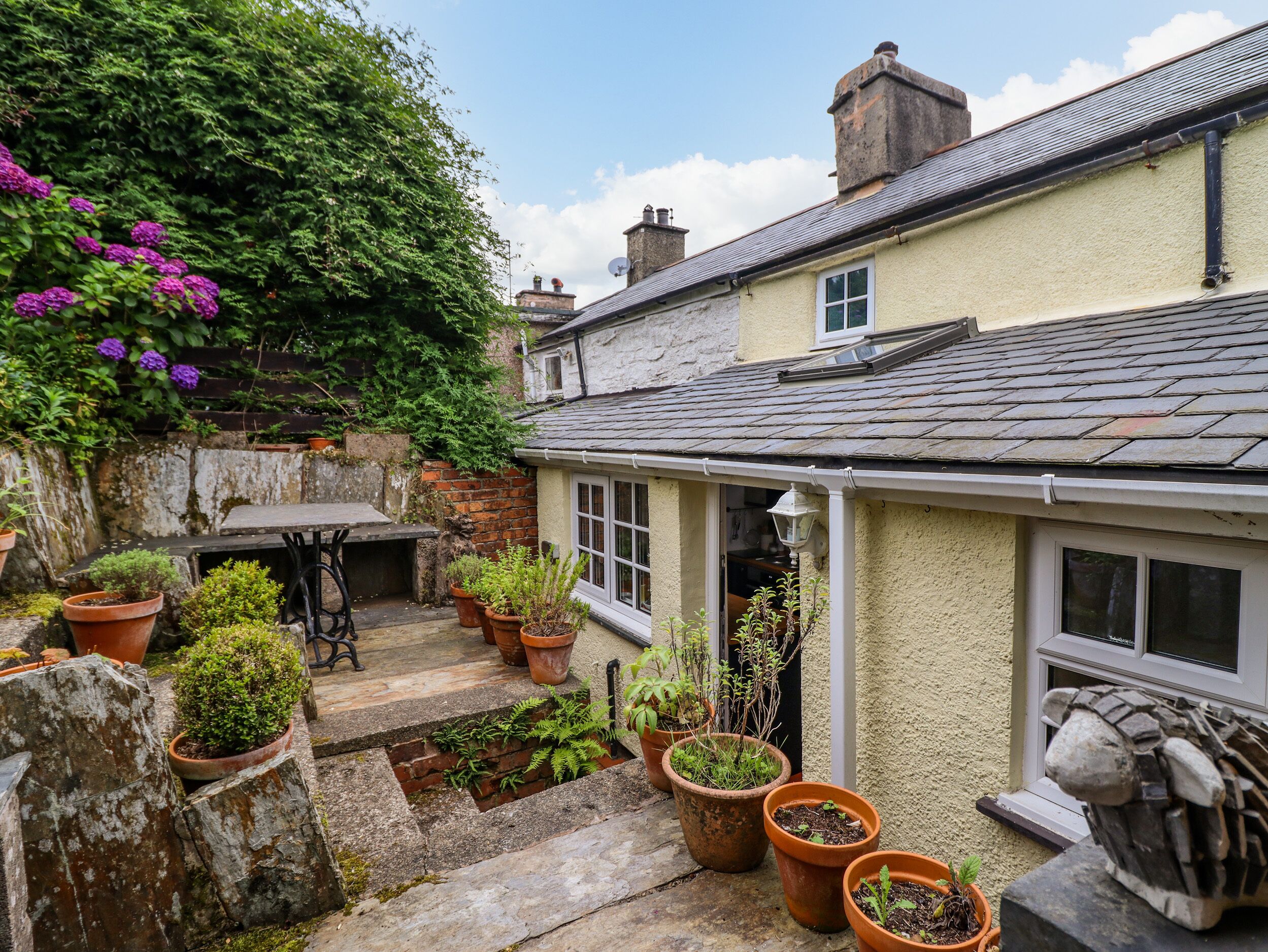 A quaint courtyard with a stone bench, potted plants, and a small table.