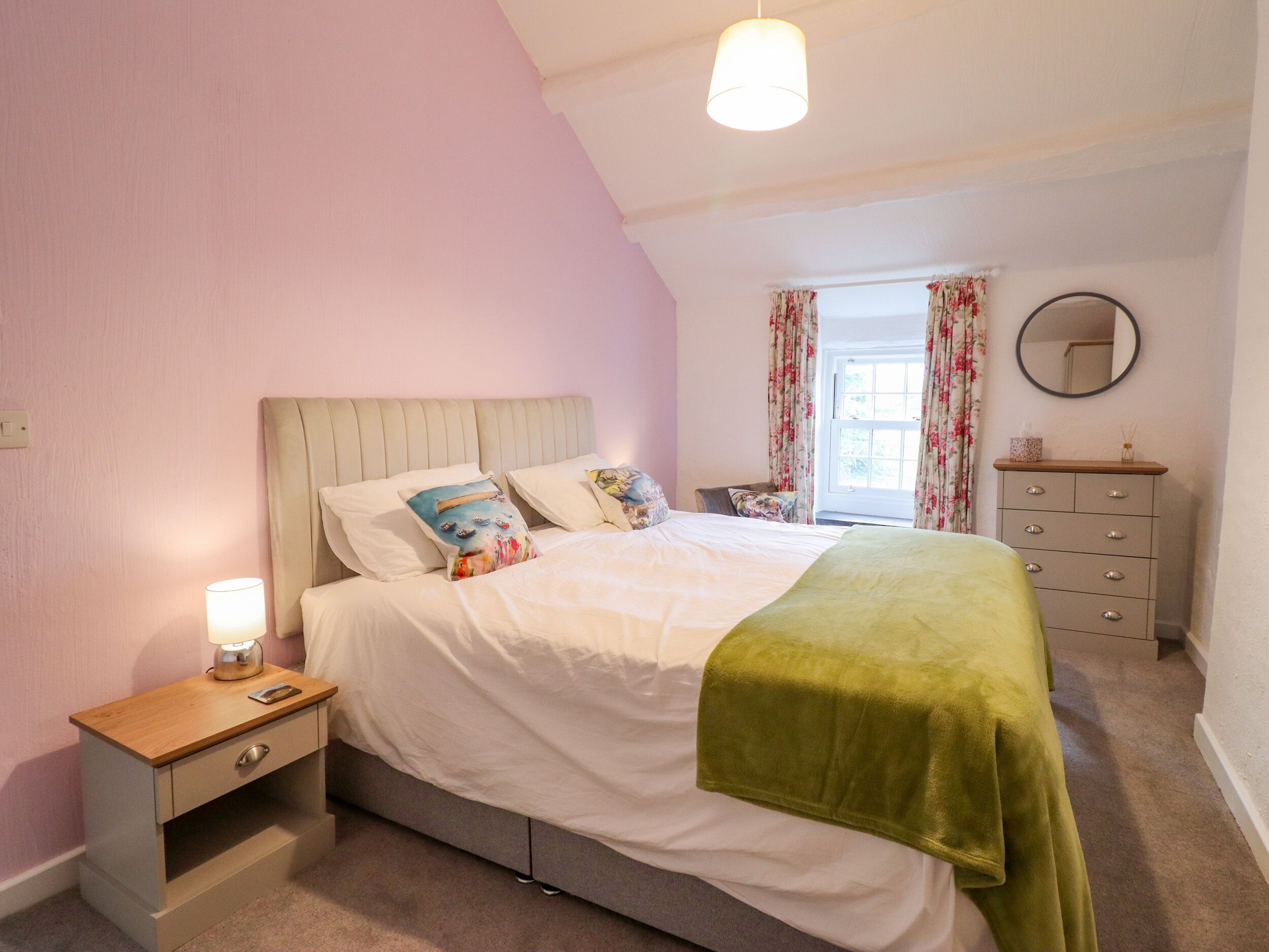 A bedroom with a bed, bedside table, dresser, and a window with curtains.