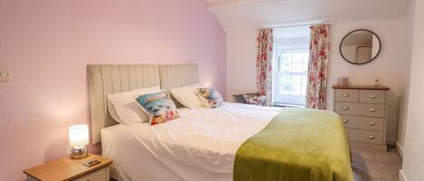 A bedroom with a bed, bedside table, dresser, and a window with curtains.