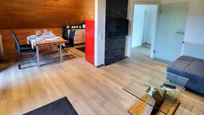 Un soggiorno moderno con soffitto in legno, un'area pranzo con tavolo apparecchiato per quattro persone, un armadietto rosso e un tavolino da caffè in vetro con un modellino di aereo.