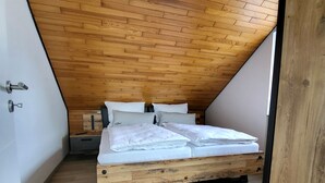 Una camera da letto con soffitto spiovente, pavimento in legno, un letto con biancheria bianca e un comodino.