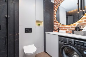 Une salle de bain moderne avec une douche en marbre, des toilettes, un lave-linge et un miroir.