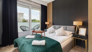 A hotel room with a bed, a nightstand, a chair, a window, and a view of buildings outside.