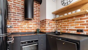A modern kitchen with a brick wall backsplash, black cabinetry, a built-in oven, and a wooden shelf above the sink.