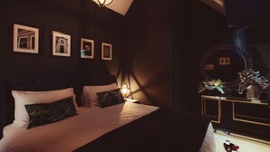 A dimly lit bedroom with a large bed, a bedside table with a mirror, and framed pictures on the wall. - Luxury Boutique 2 Bed Apartment in the heart of Bowness on Windermere (Bowness-on-Windermere)
