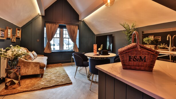 A modern loft apartment with a high ceiling, a cozy seating area with a sofa and chairs, a dining table, and a kitchen area with a wicker basket labeled "I&M". - Luxury Boutique 2 Bed Apartment in the heart of Bowness on Windermere (Bowness-on-Windermere)