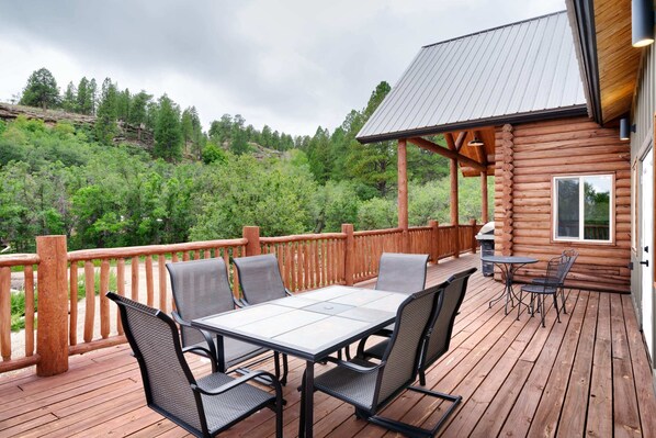 A wooden deck with a table and chairs, overlooking a forested hillside.