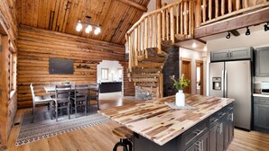 A rustic cabin interior with a wooden dining area, a kitchen with modern appliances, and a wooden staircase. - Bears Ears Luxury Retreat (Monticello)