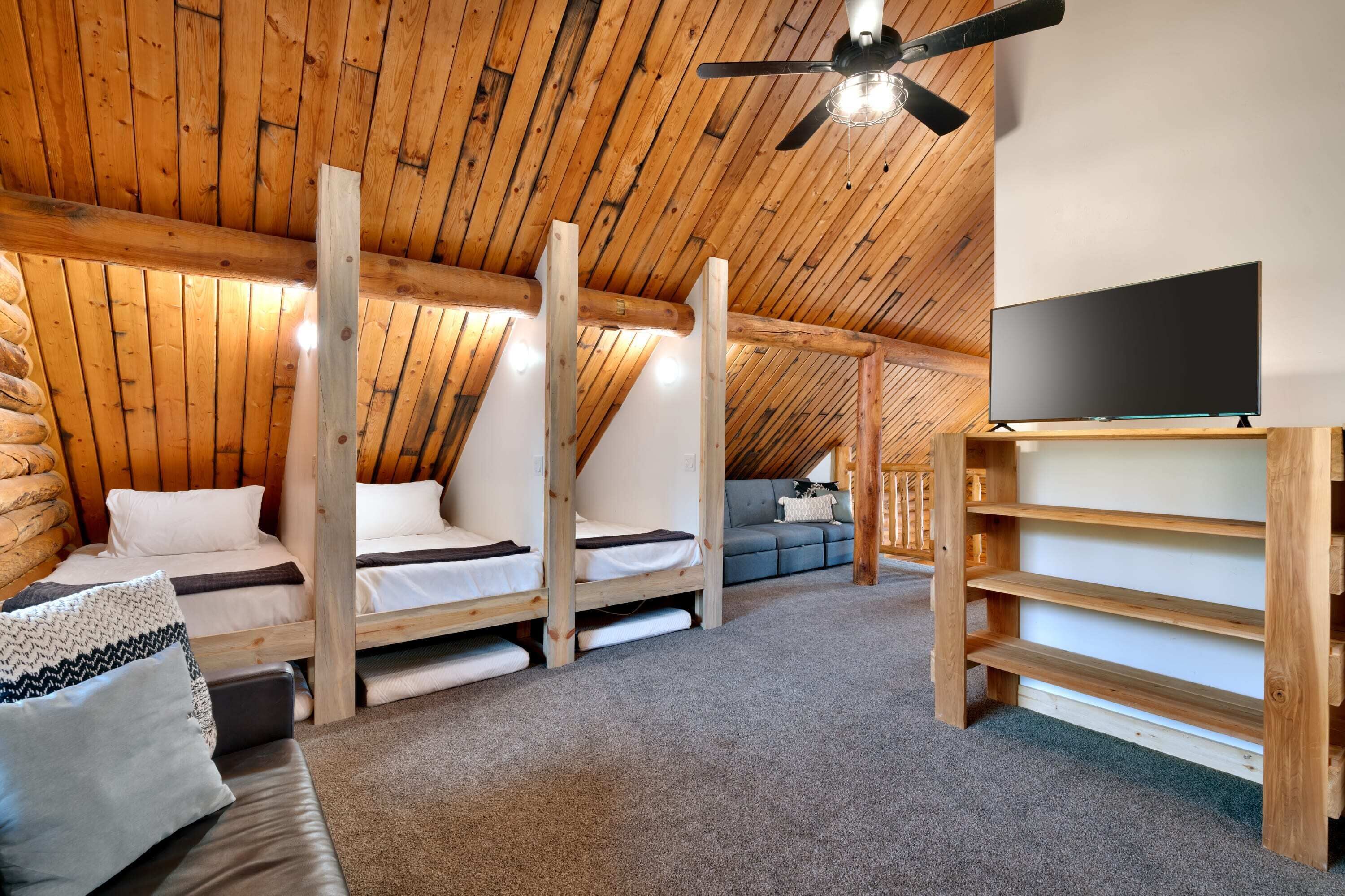 Une chambre confortable située sous les toits, avec des poutres apparentes, des lits superposés, un téléviseur à écran plat et un ventilateur de plafond.