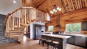 A spacious kitchen with a central island, wooden staircase, and a large window providing a view of the outdoors. - Bears Ears Luxury Retreat (Monticello)