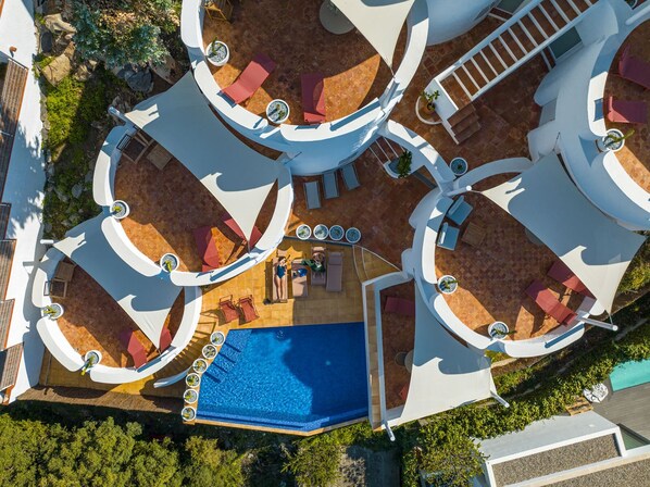 An aerial view of a resort with multiple circular outdoor seating areas, a central pool, and a staircase leading to an upper level.