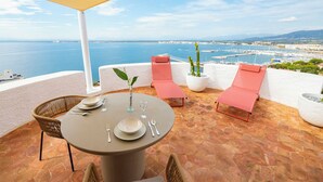A terrace with a table set for two, two lounge chairs, and a potted plant. - Agi Castell Mar 1003 Apartamento for rent in Roses Girona. (Roses)