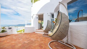 A terrace with hexagonal tiles, white walls, and a view of the city. There are two hanging chairs with patterned cushions and a hose on the floor. - Agi Castell Mar 1001 Apartamento for rent in Roses Girona. (Roses)
