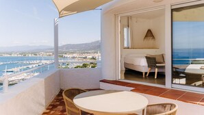 Un balcon avec une table et des chaises blanches, un canapé et une vue sur la mer et le port de plaisance.