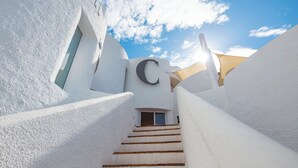 Un bâtiment aux murs blancs, avec un escalier menant à une porte sur laquelle est inscrit un grand « C ».